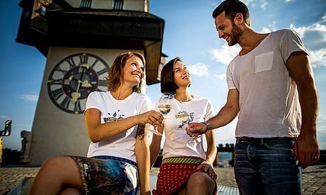 Menschen trinken Wein und genießen das Grazer Stadtleben vor dem Uhrturm